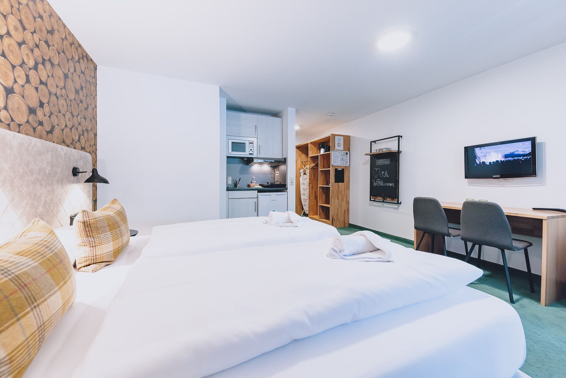 Une chambre d’hôtel avec deux lits, un bureau, une télévision, un coin cuisine et une armoire en bois.