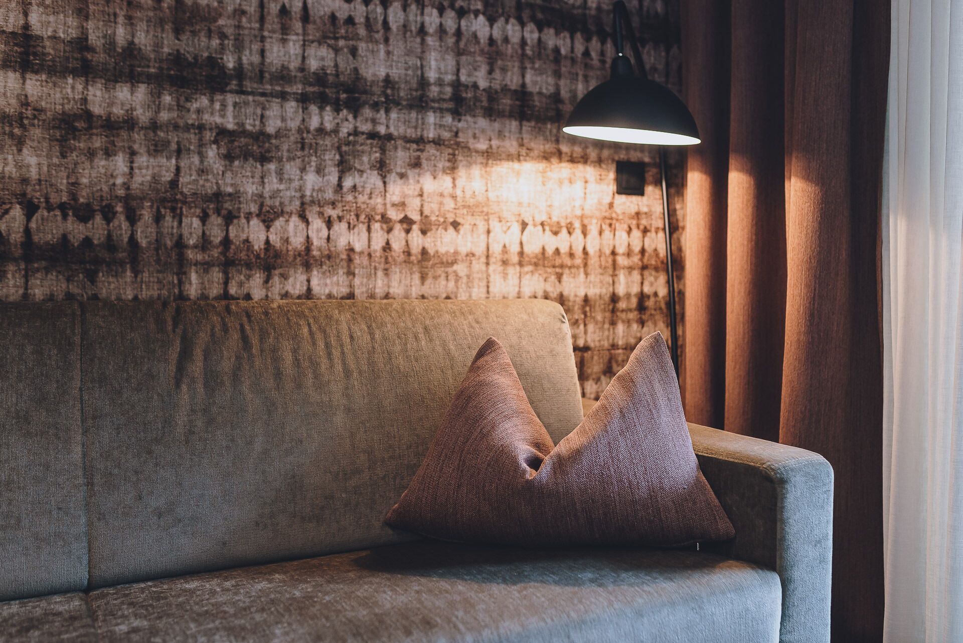 A sofa with two pillows against a textured wall, under a hanging lamp.