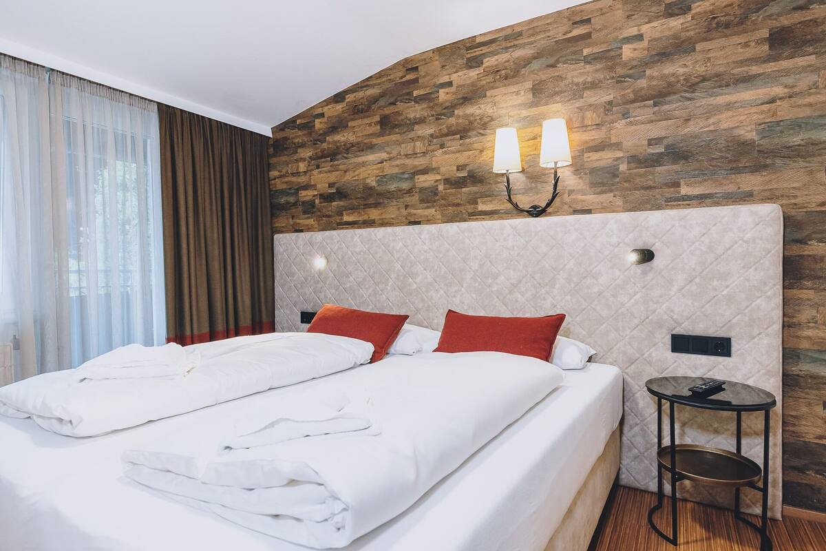 Une chambre d’hôtel avec un lit, deux tables de chevet, un mur orné d’un motif en bois et une fenêtre avec des rideaux.