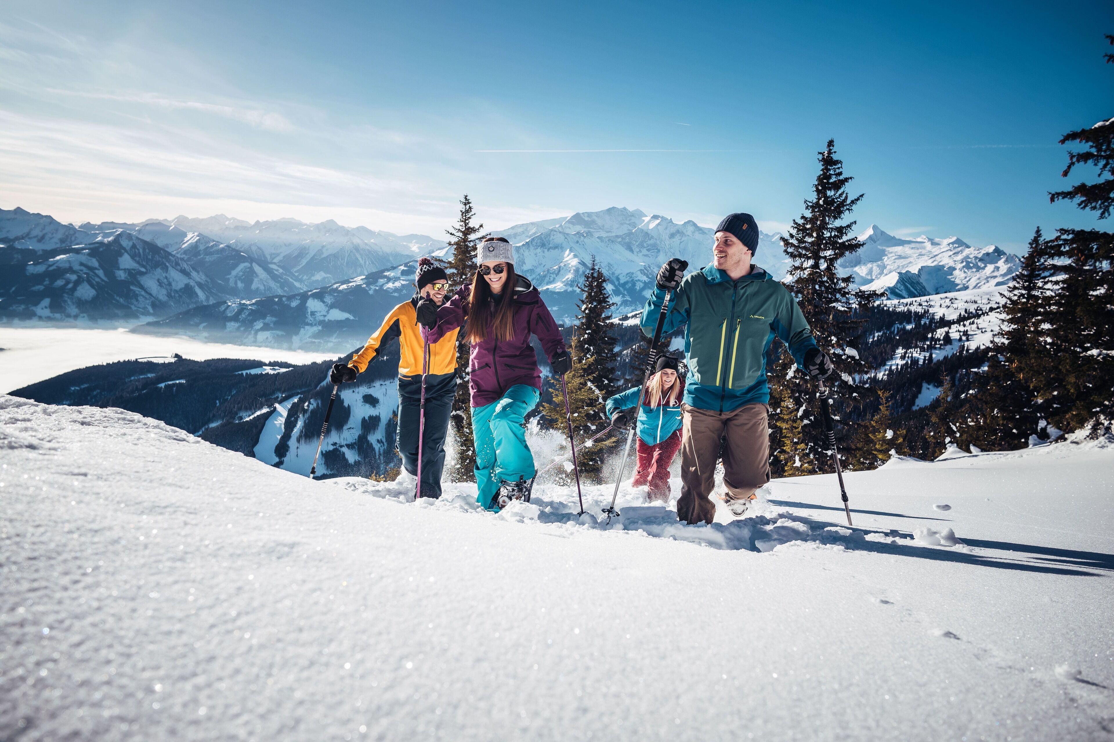 Eine Gruppe von Personen ist auf einem verschneiten Berg beim Skifahren unterwegs, im Hintergrund sind schneebedeckte Gipfel sichtbar.