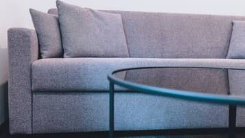 A grey sofa with a textured fabric, a glass coffee table with a metal frame, and a dark wooden floor.