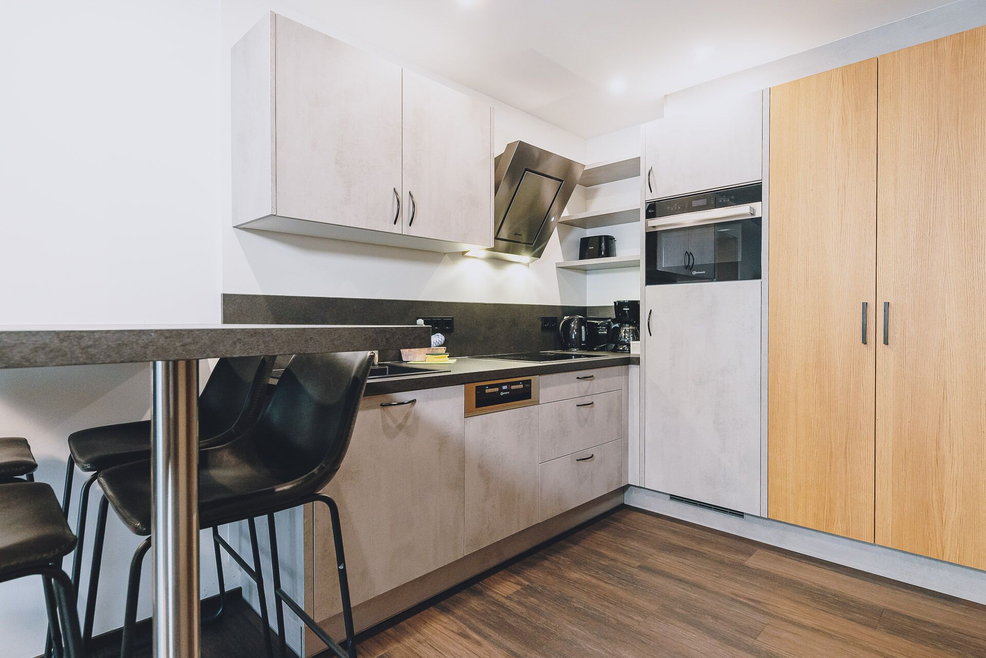 Una cocina moderna con armarios blancos, un mueble de madera, horno empotrado y cafetera.