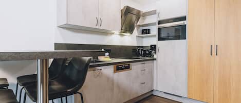 Una cocina moderna con armarios blancos, un mueble de madera, horno empotrado y cafetera.
