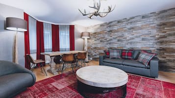 Een moderne woonkamer met een stenen muur, een ronde salontafel, een bank met geruite kussens, een eettafel met stoelen en een kroonluchter.