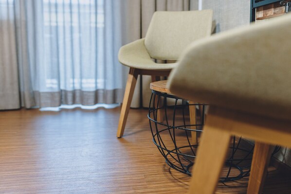 A wooden floor, a chair with a woven base, and a window with curtains.