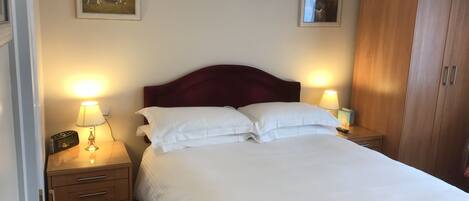 A neatly made bed with white linens, two bedside tables with lamps, a wooden wardrobe, and two framed pictures on the walls.