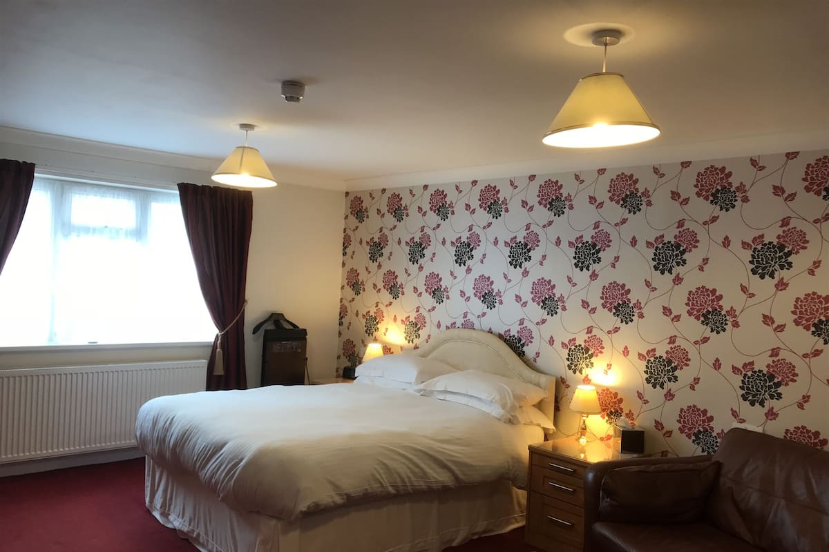 A hotel room with a bed, a nightstand, a lamp, a sofa, and a window with curtains.