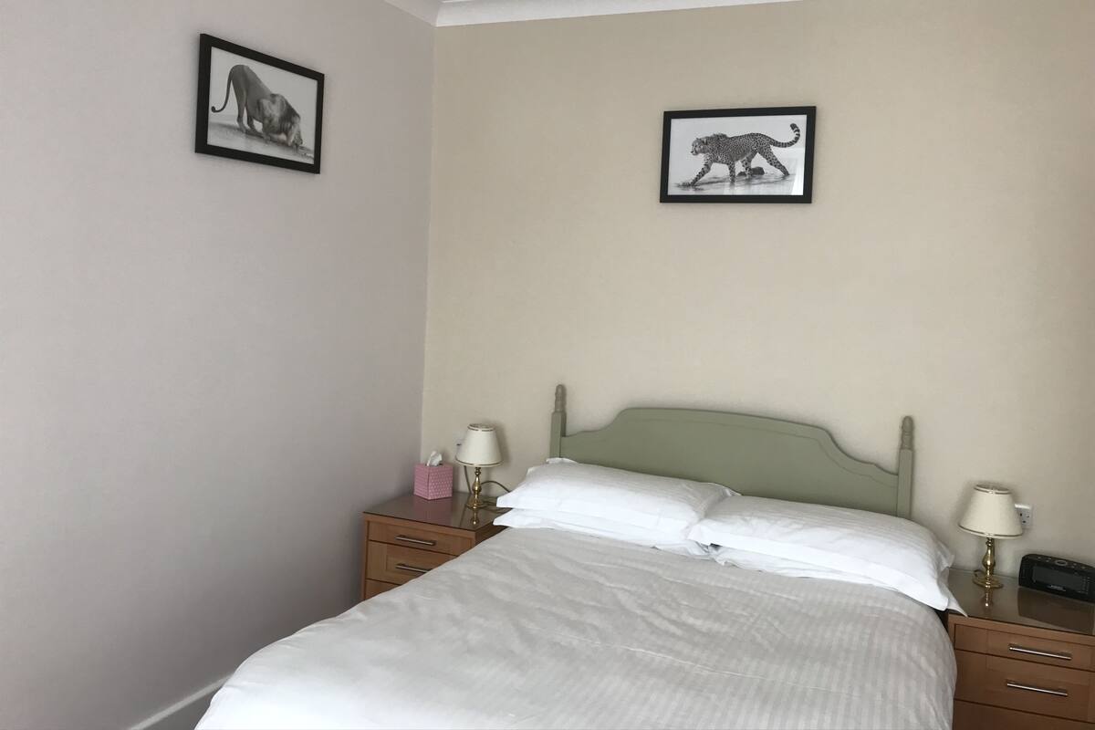 A neatly made bed with white linens, a wooden nightstand with a lamp, and two framed animal pictures on the wall.