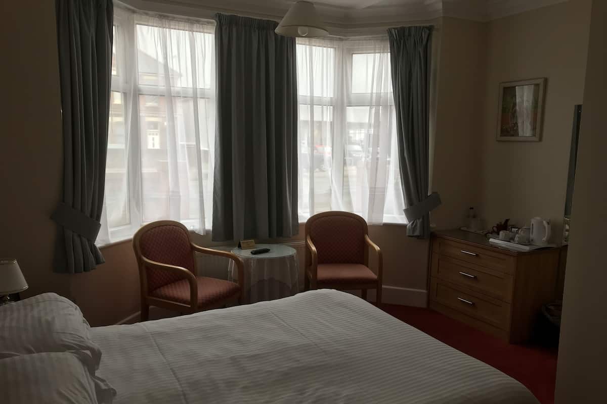 A hotel room with a large bed, two armchairs, a small table, a dresser, and a painting on the wall.