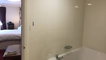 A bathroom with a bathtub, a towel rack, and a small table with a book.
