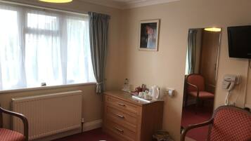 Une chambre d’hôtel comprenant un lit, une commode en bois, un miroir, un radiateur, une fenêtre avec des rideaux et un téléviseur.