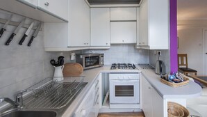 Een kleine keuken met witte kastjes, een magnetron, een gasfornuis en een afdruiprek.