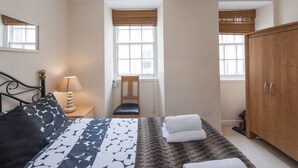 Een slaapkamer met een bed, nachtkastje, lamp, stoel, kast en ramen.