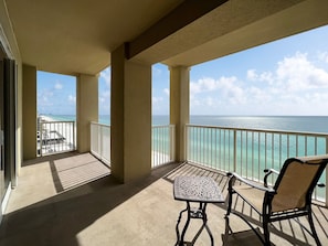 A balcony with a view of the ocean, a table, and two chairs.
