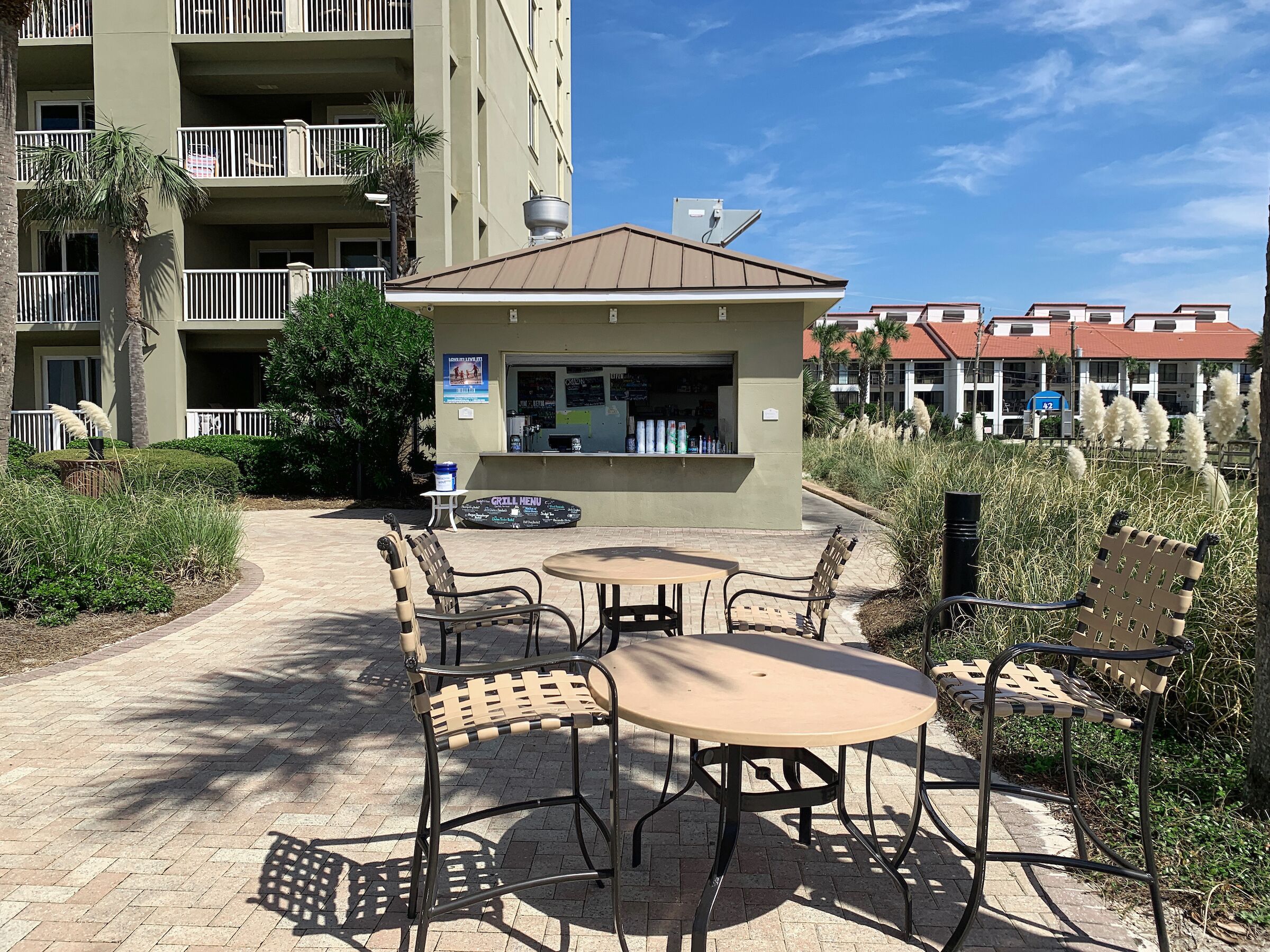 Un espace extérieur aménagé en terrasse avec une table et des chaises, un panneau indiquant le menu du barbecue, et un bâtiment avec des balcons en arrière-plan.