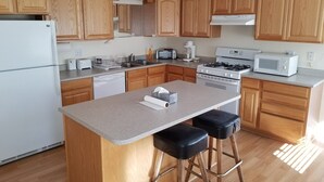 A modern kitchen with wooden cabinets, a central island with stools, a refrigerator, a stove, a microwave, and a dishwasher.