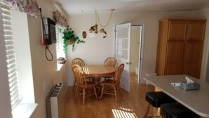 A dining area with a wooden table and chairs, a kitchen counter with a tissue box, and a window with blinds.