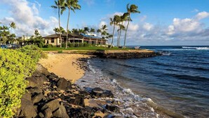A beachfront property with a large house, palm trees, and a rocky shoreline. - Ocean View Ground floor Suite Steps to the sand, water and in sunny Poipu (Koloa)