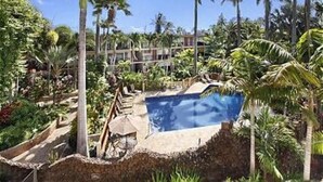 A pool surrounded by palm trees and a building with multiple balconies. - Ocean View Ground floor Suite Steps to the sand, water and in sunny Poipu (Koloa)