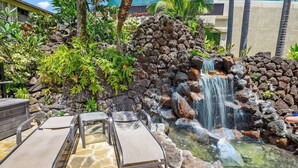 A pool area with lounge chairs, a waterfall, and surrounding tropical vegetation. - Ocean View Ground floor Suite Steps to the sand, water and in sunny Poipu (Koloa)