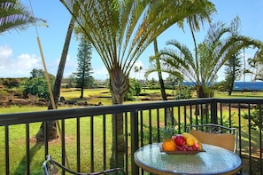Enjoy a serene ocean view from this balcony, featuring a wicker chair and a table set with a fresh fruit bowl.