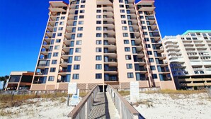 Un hôtel à plusieurs étages doté de balcons, offrant une vue sur la plage et comprenant une passerelle en bois menant à l’entrée.