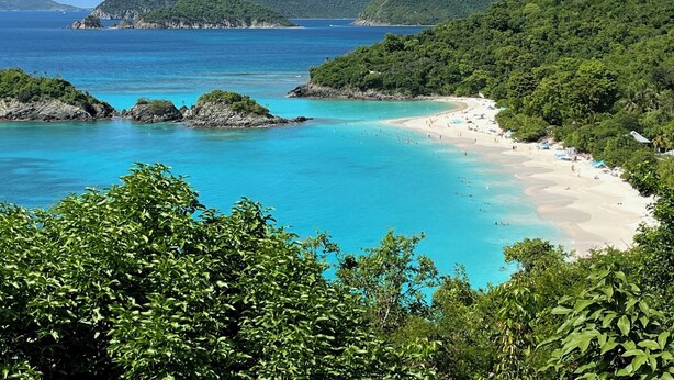 Una playa con aguas turquesas cristalinas, rodeada de colinas verdes exuberantes.