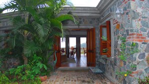 Un edificio de piedra con un patio empedrado, plantas en macetas y vistas al mar.
