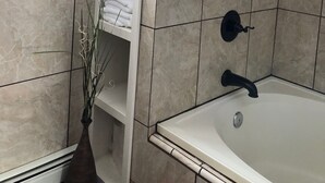 A bathroom with a bathtub, a shelf with towels, and a window with curtains.
