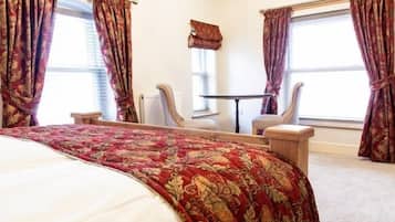 Ein Hotelzimmer mit einem großen Bett, zwei Stühlen, einem kleinen Tisch und einem Fenster mit Vorhängen.