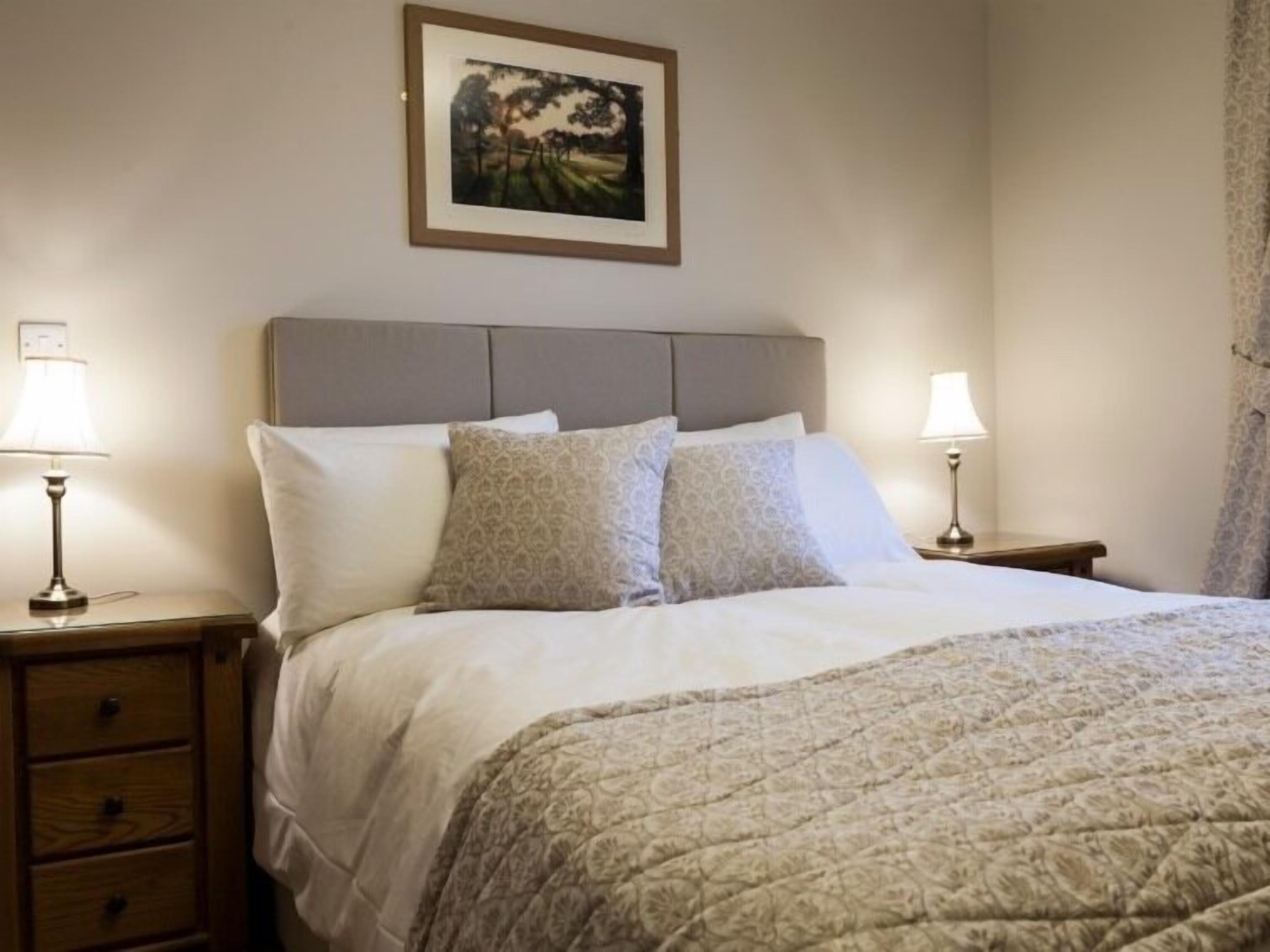 A neatly made bed with a patterned quilt, two bedside lamps, and a framed picture on the wall.