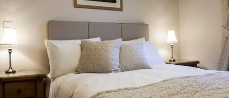Una cama bien hecha con colcha estampada, dos lámparas de noche y un cuadro en la pared.
