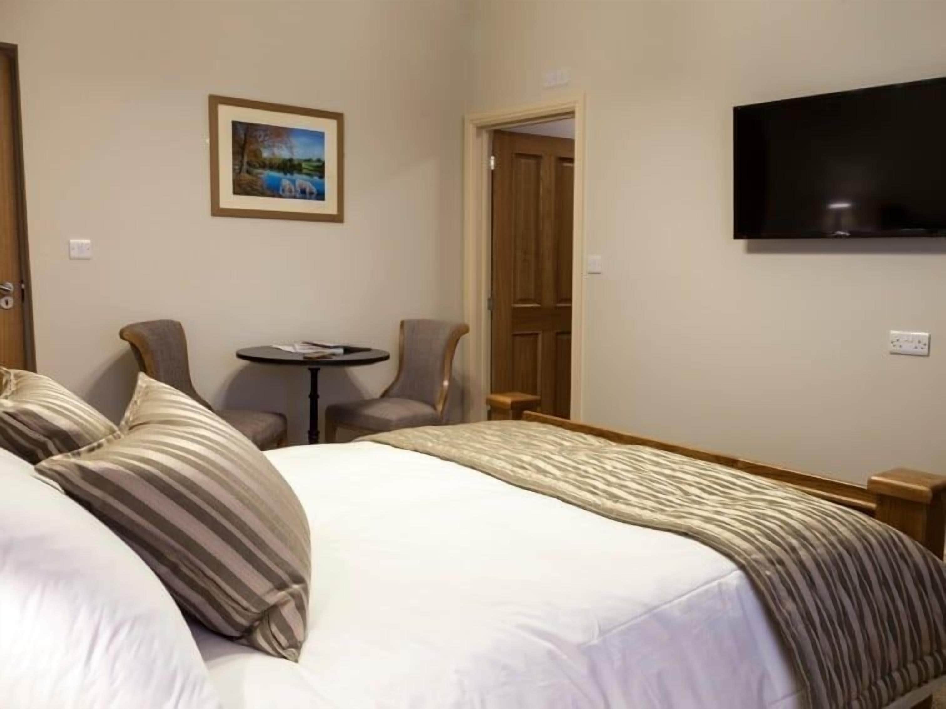 Een hotelkamer met een groot bed, twee fauteuils, een klein rond tafeltje, een televisie en een deur die naar een andere kamer leidt.