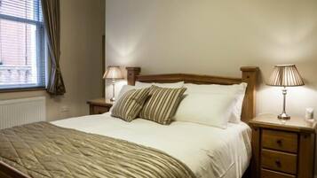 A neatly made bed with a striped blanket, two bedside lamps, and a wooden nightstand with drawers.