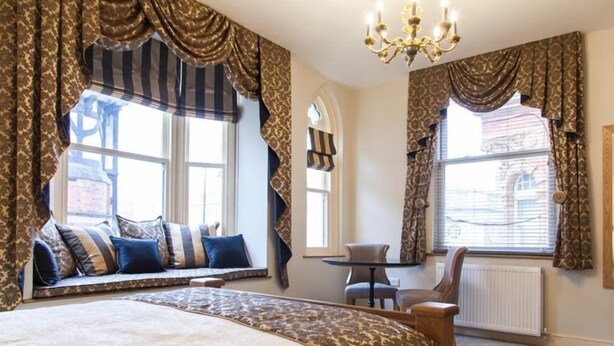 A bedroom with a large bed, a window seat with cushions, a small table, and a chair.