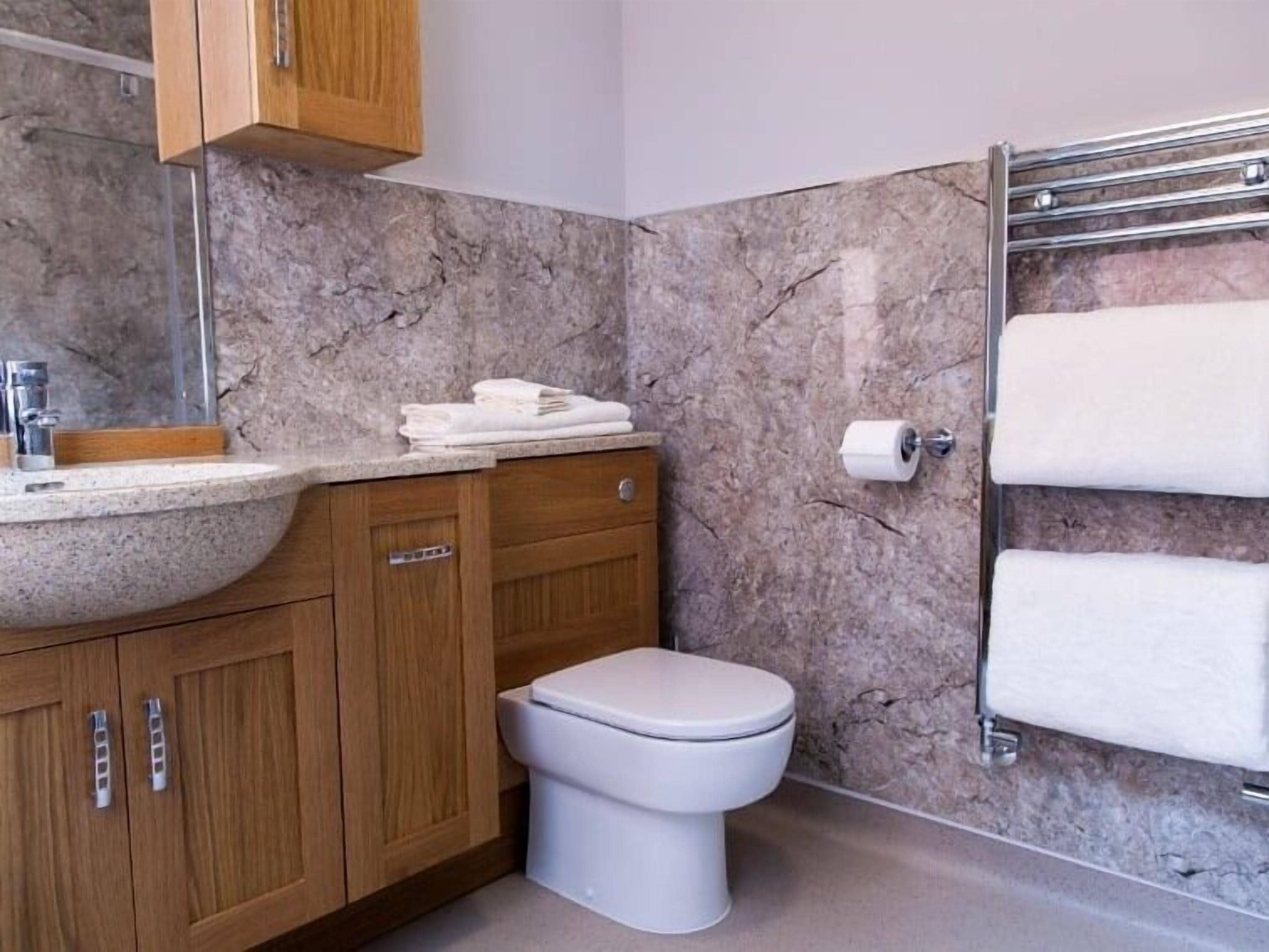 A bathroom with a marble sink, wooden cabinets, a toilet, and a towel rack.