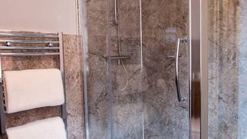A glass-enclosed shower with a marble wall, a towel rack with two towels, and a showerhead.