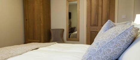 A bedroom with a bed, a wooden wardrobe, a chair, and a door.