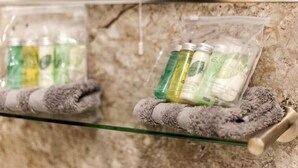 A bathroom with a glass shelf holding toiletries and a towel.