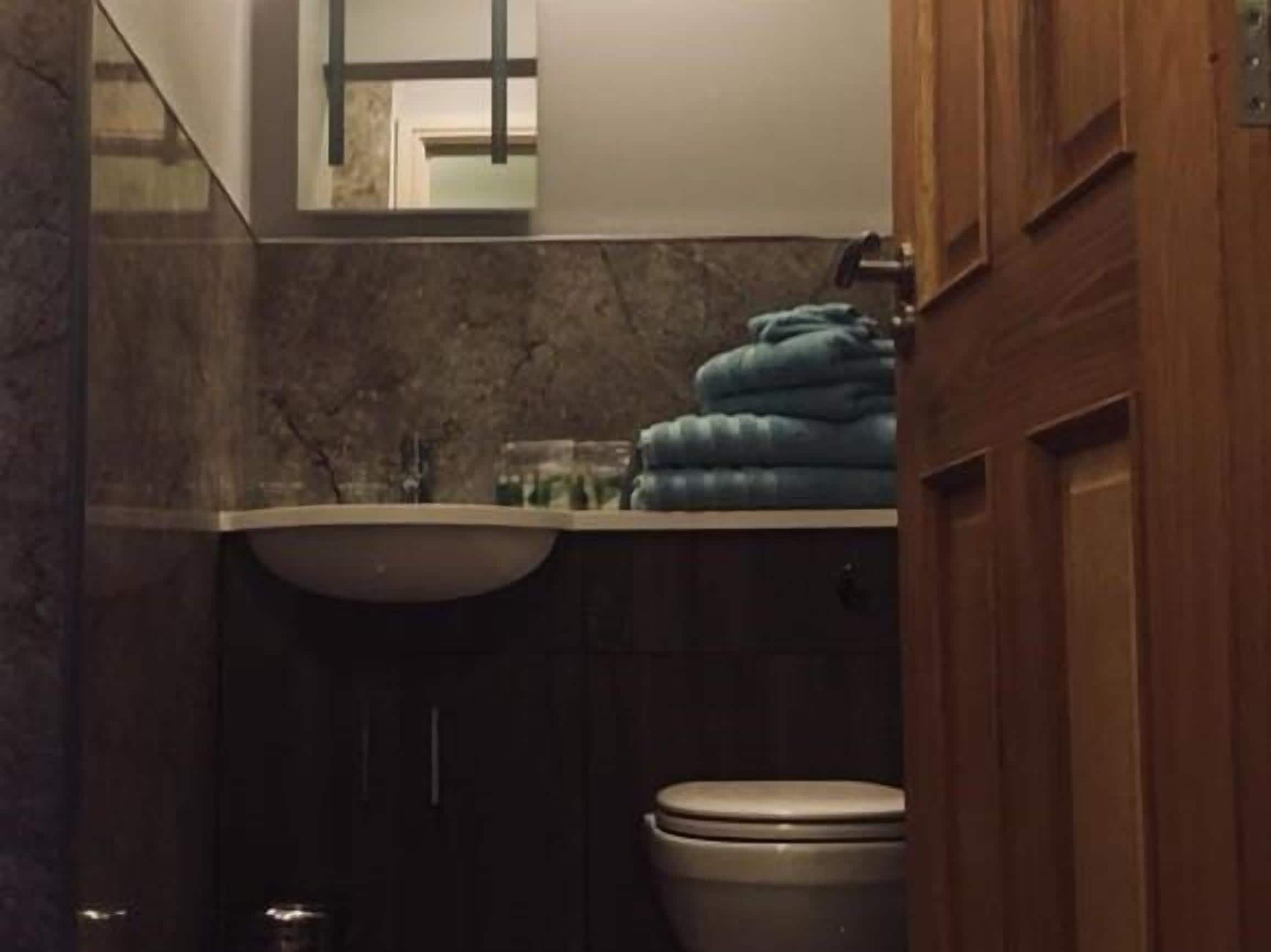 A bathroom with a marble wall, a sink, a mirror, and a toilet.