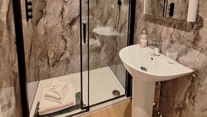 A modern bathroom with a glass-enclosed shower, a pedestal sink, and marble walls.