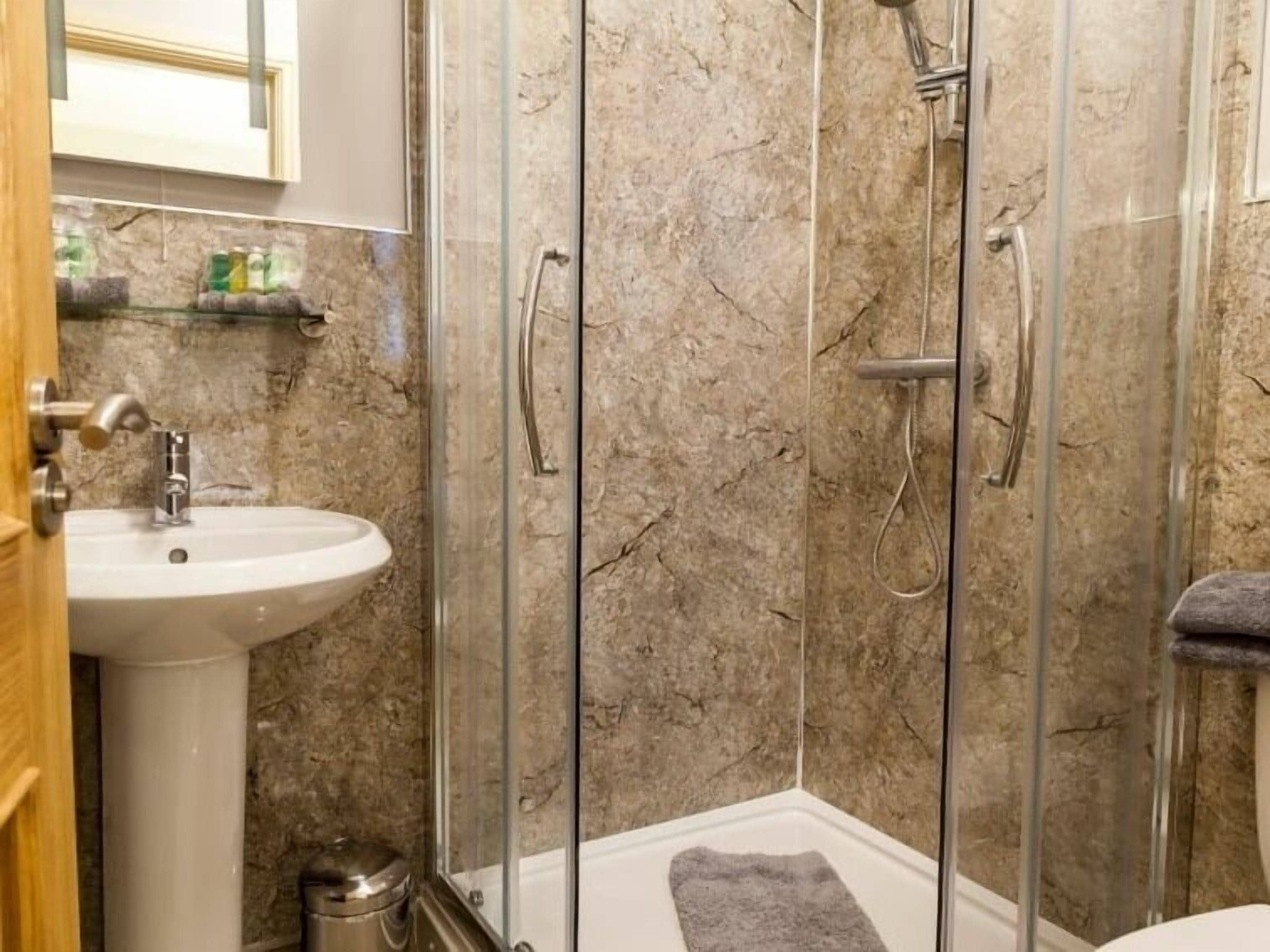 A bathroom with a glass-enclosed shower, a sink, and a marble wall.
