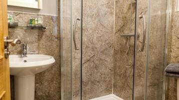 A bathroom with a glass-enclosed shower, a sink, and a marble wall.