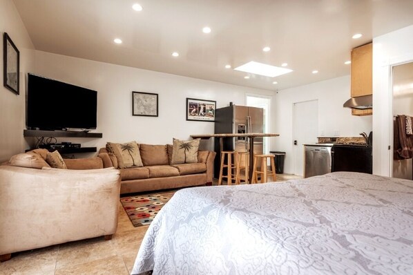 A modern bedroom with a large bed, a sofa, a TV, and a kitchenette.