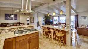 Una cocina amplia con una isla central, taburetes de madera y luces colgantes.