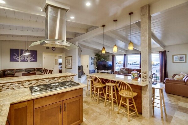 A spacious kitchen with a central island, wooden bar stools, and pendant lighting.