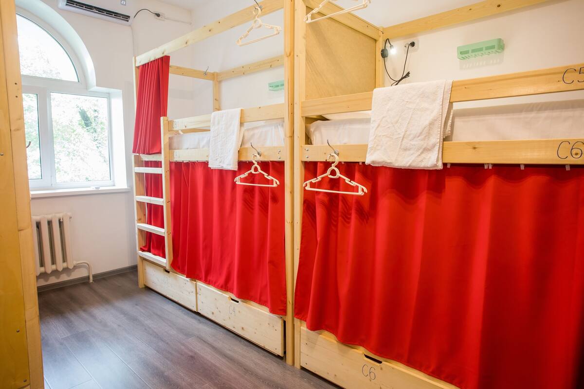 Une chambre de dortoir avec des lits superposés, des rideaux rouges et un radiateur.