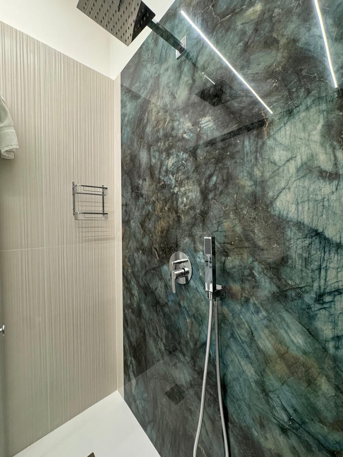A modern bathroom with a marble wall, a shower with a handheld showerhead, and a towel rack.