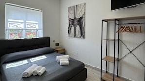 A modern bedroom with a large bed, a TV, a wardrobe, and a window with a view of a bridge. - Beatrice Home B&B (Pompei)