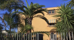 A building with a yellow facade, surrounded by palm trees and a metal fence. - Beatrice Home B&B (Pompei)